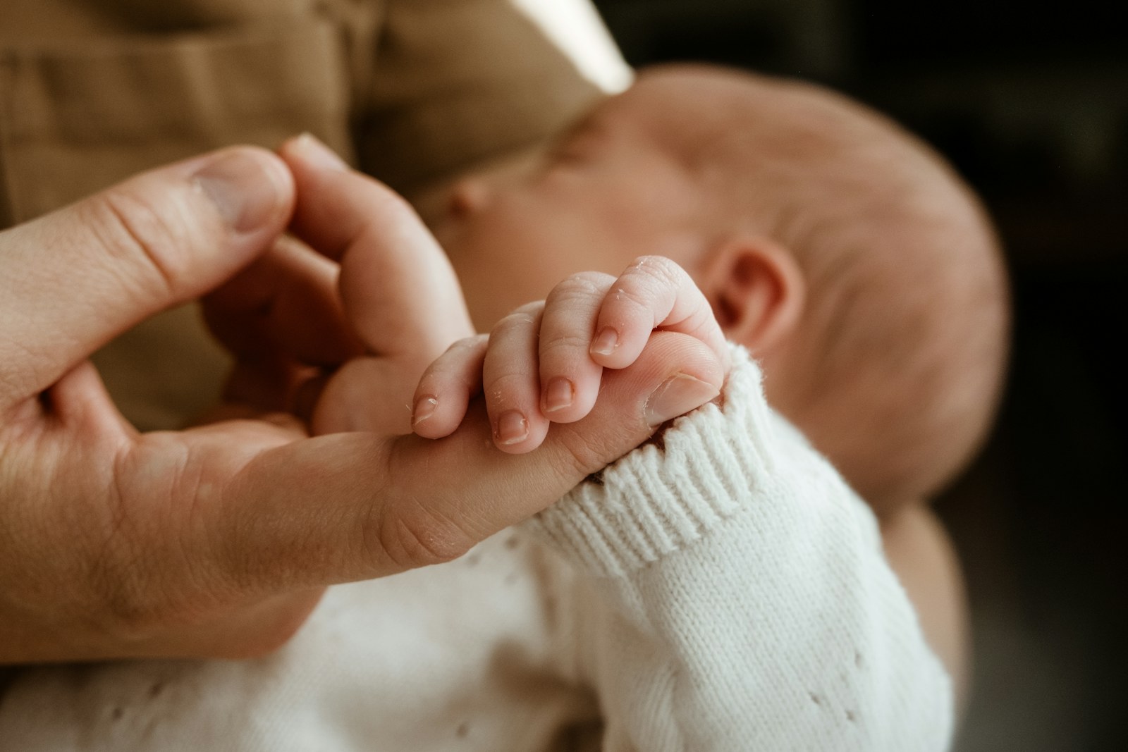 Adult hand gently holding a newborn baby's hand